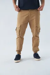 Pantalón cargo color beige, corte slim, con bolsillos laterales con botón, cierre con botón y puños en los tobillos.