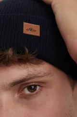 Gorro de punto inglés en color azul marino, con diseño de doble capa y etiqueta de cuero sintético con logo en el frente.