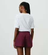 Short pollera de sastrería marca Cortelle, color bordó, confeccionado en crepé. Presenta sobreposición frontal efecto pollera con pliegues y detalle de cadena metálica decorativa en el lateral.