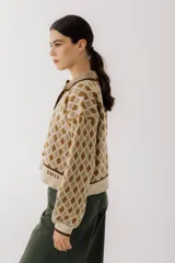 Buzo de tejido de punto con diseño de rombos en tonos beige y marrón. Presenta cuello polo con cierre frontal de tres botones, mangas largas con puños acanalados y ruedo también acanalado.