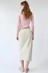 Falda midi de tiro medio color beige, con pliegues en la parte delantera, abertura frontal en el bajo y cinturón combinado a tono con hebilla metálica.