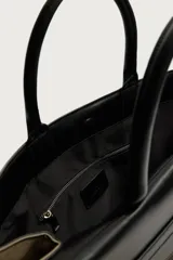 Bolso shopper de mano combinando cuerpo de gamuza color verde militar con solapa superior, asas y detalles en cuero sintético negro. Cuenta con compartimento principal con cierre imantado, bolsillo interior con cierre y bolsillo frontal plano con solapa.