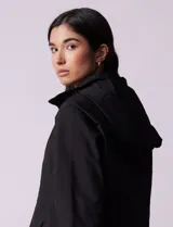 Campera impermeable color gris claro, marca Gallery. Tiene abertura central con cierre oculto y botones a presión, bolsillos delanteros y capucha plegable en el cuello.
