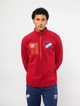 Buzo de micropolar azul con medio cierre frontal, cuello alto y bolsillo con cierre en el pecho. Presenta el logo de Umbro y el escudo del Club Nacional de Football.