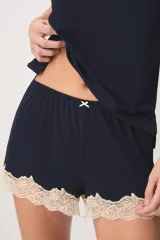 Pijama de dos piezas color verde menta, confeccionado en poliamida y elastano. Incluye una musculosa con tirantes finos y detalles de encaje beige en el escote, y un short con cintura elástica, pequeño lazo decorativo y apliques de encaje en los ruedos.