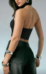 Top negro tipo bandeau, ajustado al cuerpo, con cuello tipo choker incorporado que se une al centro del busto mediante una argolla metálica plateada.
