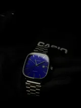 Reloj Casio con caja cuadrada de bordes redondeados, esfera azul vibrante con índices plateados y ventana de fecha. Cuenta con malla de eslabones de acero inoxidable y movimiento de cuarzo.