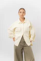 Sobrecamisa de gabardina liviana color crema, con corte oversize, cuello clásico, cierre frontal con botones a presión y dos bolsillos delanteros con solapa.