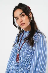 Vestido largo a rayas verticales azules y blancas, con manga globo y diseño de nido de abeja con hilo elástico hasta la cintura. Cuello alto fruncido y falda amplia con caída fluida.