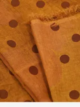 Bufanda rectangular color ocre con lunares marrones y flecos en los extremos.