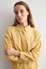 Camisa amarilla de manga larga con detalles bordados y calados en los hombros, pecho y mangas, corte clásico con cuello camisero y cierre frontal de botones.