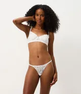 Kit de dos bombachas colaless tipo string confeccionadas en encaje floral, una en color negro y otra en color blanco. Presentan laterales finos regulables con tirantes elásticos y un pequeño dije metálico dorado en la parte frontal.