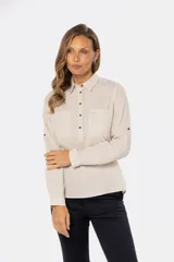 Camisa blanca de manga larga con cuello y tapeta de medio botón. Presenta dos bolsillos frontales con tapa y botones metálicos. Las mangas tienen presillas para sujetar el puño enrollado.