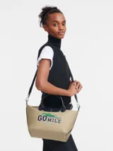 Bolso tote Longchamp modelo Le Pliage Collection S, color arena con detalles en azul marino. Presenta estampado frontal con el texto "Go the extra mile" y el logo de la marca. Incluye doble asa corta y correa larga extraíble.