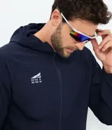 Chaqueta deportiva masculina de color azul marino, confeccionada en tejido técnico repelente al agua con acabado texturizado. Presenta cierre frontal con cremallera, capucha integrada y estampado de coordenadas en el pecho.