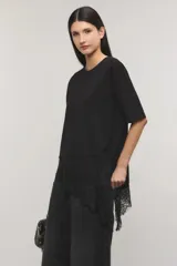 Remera negra de corte oversize, con escote redondo, mangas cortas y detalle de tajo irregular con terminación en puntilla en el ruedo. Confeccionada en jersey de algodón.
