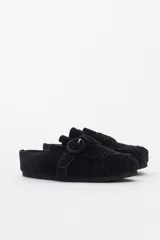 Slipper de gamuza negra con diseño destalonado, costura fruncida en la puntera y tira lateral con hebilla revestida.