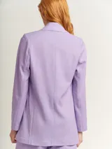 Blazer oversized lila de corte recto, largo a la cadera, con hombreras finas forradas, costuras internas con sesgo combinado y maxi bolsillos delanteros. Incluye lazo de algodón con detalle a tono.