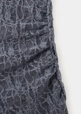 Top de encaje gris oscuro con diseño semitransparente, cuello asimétrico de hombro descubierto y manga larga.