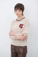 Buzo de tejido de punto color beige con cuello redondo en contraste marrón. Presenta un estampado sutil en tono sobre tono y un aplique bordado de una flor en el pecho.