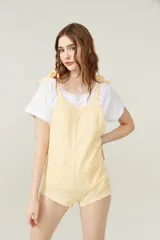 Mono corto color amarillo pastel, con breteles finos que se atan en los hombros, escote recto y dos bolsillos delanteros.