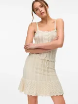 Pollera corta tejida en punto calado, color beige, con tiro medio, cintura elástica con cordón ajustable y ruedo con volado.