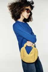 Bolso de mano de piel color verde mostaza, con cuerpo fruncido, asa de mano con detalle retorcido, cadena metálica opcional para función bandolera y cierre mediante cremallera.