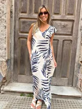 Vestido largo de corte holgado y fluido, con estampado de hojas tropicales en tonos azul marino y celeste sobre base cruda. Cuenta con escote en V y mangas cortas tipo volante.