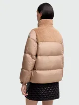 Campera de plumas corta, color beige, con cierre frontal y cuello alto de tejido tipo borrego en tono camel. Presenta hombros y cuello con apliques de borrego.