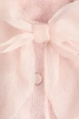 Saco de punto suave color rosado, de manga corta y cuello redondo. Presenta cierre frontal con botones forrados y una moña decorativa de organza transparente en la parte superior. Posee terminaciones acanaladas en mangas y ruedo.