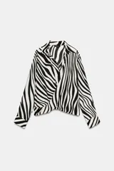 Camisa de manga larga con estampado de cebra, cuello solapa, escote en pico y cierre frontal con botones. Presenta un diseño con nudo en el bajo delantero y puños abotonados.