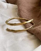 Brazalete rígido de diseño minimalista con forma de espiral, elaborado artesanalmente en bronce y alpaca maciza. Es una pieza ajustable que puede lucirse tanto en el antebrazo como en la parte superior del brazo.