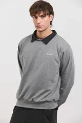 Buzo de algodón rústico color gris melange, con cuello redondo y cuello tipo polo negro superpuesto. Presenta el logo de la marca bordado en el pecho y puños acanalados.