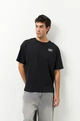 Remerón unisex de manga corta, color negro, con cuello a la base. Presenta una pequeña inscripción lateral en el pecho y un gran estampado en la espalda.