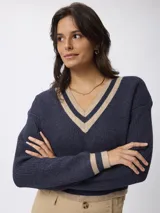 Sweater de punto estilo preppy, color blanco con detalles de rayas negras en el escote en V, puños y ruedo. De corte holgado y manga larga.