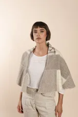 Chaleco sin mangas de tejido de lana fina sin teñir, con diseño circular y bloques de color beige y marrón. Presenta un cuello amplio y solapa que permite usarlo como chaleco largo o capa corta.