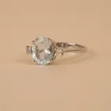 Anillo solitario de oro blanco 18k con una piedra central de aguamarina en corte ovalado y pequeños brillantes laterales engarzados en cuatro puntas.