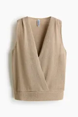 Top de punto sin mangas, color beige, con diseño cruzado en el frente, escote en V pronunciado y pliegues en los hombros. Presenta un dobladillo acanalado.