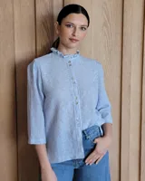 Camisa de manga tres cuartos color beige con cuello con volados y botones frontales. Presenta un detalle de color negro en la parte superior de las mangas.