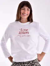 Remera de manga larga color crema con cuello redondo y un estampado central de un ramo de flores rosadas y naranjas en un jarrón azul oscuro.