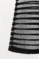 Top negro con cuello halter ajustable mediante lazo. La parte superior es opaca y ajustada, mientras que la parte inferior presenta un tejido semitransparente con franjas horizontales en relieve.