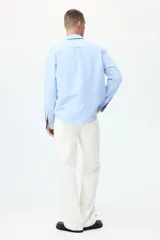 Camisa de algodón Oxford con cuello americano, bolsillo frontal y mangas largas con puños abotonados. Presenta un corte estándar con bajo redondeado.