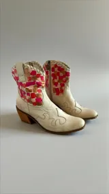 Botas de cuero estilo texano color natural, con caña corta decorada con un diseño artístico de cuadrados en tonos coral, fucsia y marrón. Presentan costuras decorativas en la puntera y un taco cuadrado de madera.
