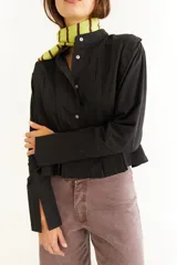 Blusa blanca de algodón con cuello mao y tablas verticales en el frente que crean un efecto de volumen. Presenta cierre frontal con botones y mangas largas.