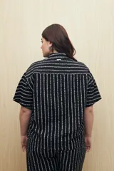 Conjunto de camisa y pantalón a rayas verticales en blanco y negro. La camisa es de manga corta, confeccionada en viscosa suave y fluida, con cuello clásico y botones al frente. El pantalón es de corte palazzo, con cintura alta y pernera ancha.