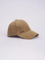 Gorra de béisbol confeccionada en pana color beige, con detalle de placa metálica con logo de la marca en el lateral.