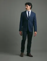 Saco de vestir azul marino con cuello solapa, manga larga y cierre frontal de dos botones. Presenta un diseño clásico con bolsillos laterales con solapa y un bolsillo superior en el pecho.