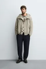 Parka de tejido técnico con acabado engomado, cuello subido y capucha ajustable. Presenta cierre frontal con cremallera oculta bajo solapa con botones a presión, bolsillos laterales de vivo y mangas largas con puños ajustables.