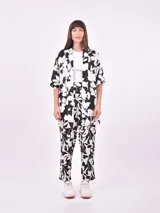 Pantalón babucha de tiro alto con cintura fruncida y lazo para ajustar. Estampado de hojas tropicales en tonos naranja y marrón sobre fondo blanco.