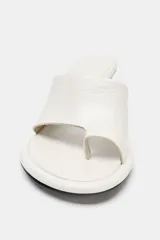 Sandalia tipo mule de tacón alto fino de madera, confeccionada en piel color blanco marfil. Presenta una tira asimétrica con separador para el dedo y punta redonda.